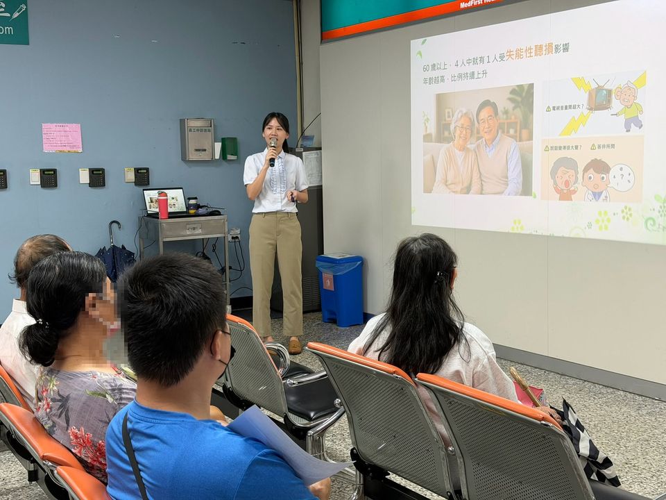 聽力師向候診的民眾講解「老年性聽力損失」，投影幕上說明 60 歲以上每 4 人就有 1 人受失能性聽損影響